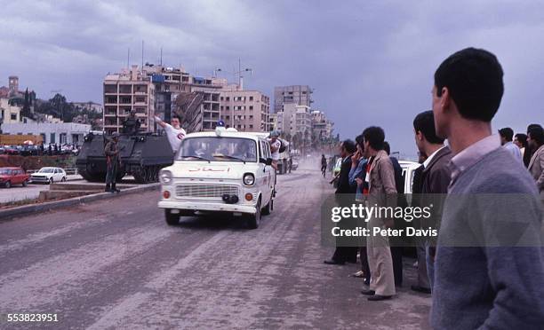 The collapsed facade of the American Embassy building is visible in the background as an ambulance drives past a crowd of onlookers, on the day of...