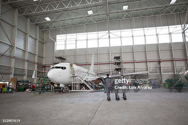 engineers walking towards airplane in hangar - hangar stockfoto's en -beelden