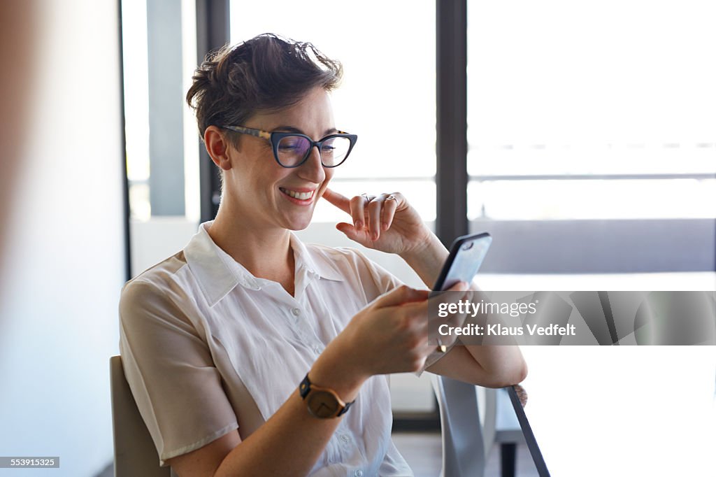 Cool businesswoman looking at phone and laughing