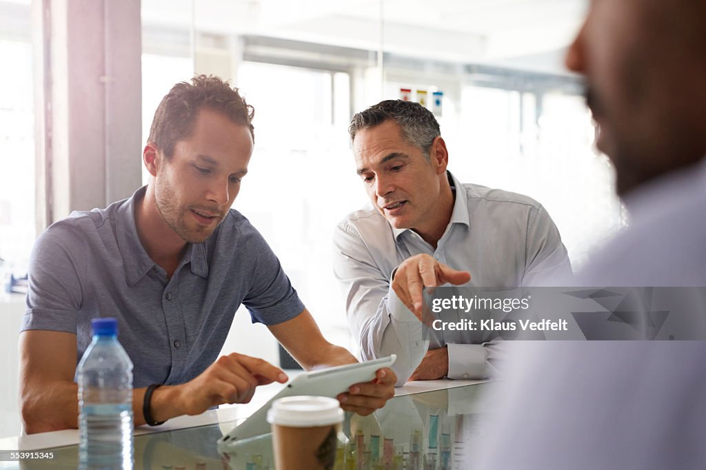 Businessmen looking at tablet at meeting