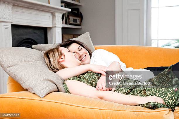 lesbian couple cuddling on the sofa - leaninlgbt stock pictures, royalty-free photos & images