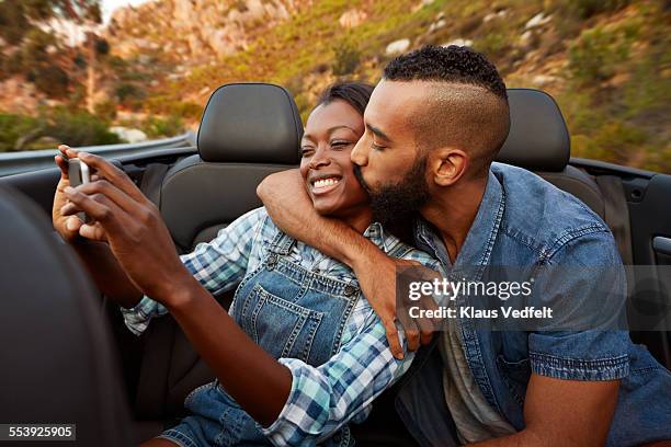 couple kissing while making selfie in car - friends kissing cheeks fotografías e imágenes de stock