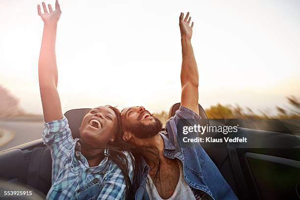 couple in convertible car laughs with arms raised - driver rider stock pictures, royalty-free photos & images