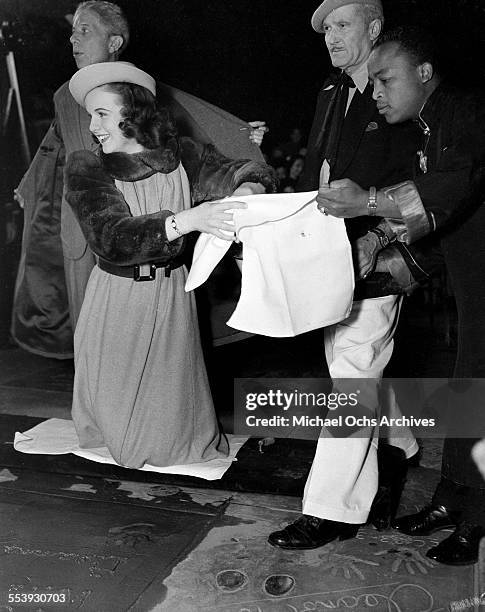 Actress Deanna Durbin wipes off her hands after making a hand print in cement in front of Grauman's Chinese Theater with the help of Jean W. Klossner...