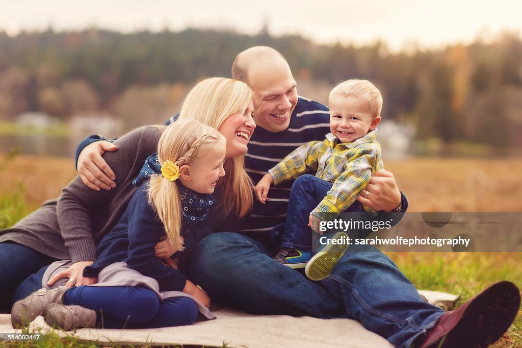 Blond family of four sitting outside laughing