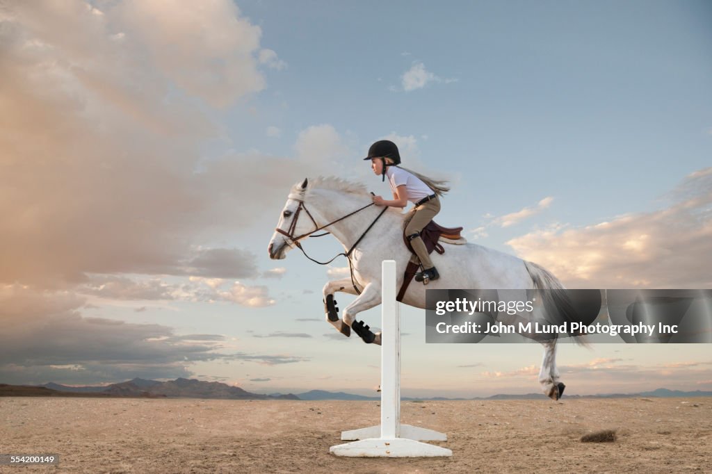 Caucasian girl riding horse over gable in race
