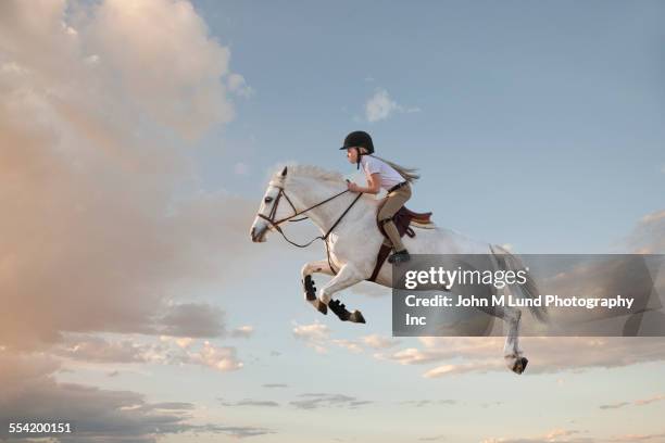 caucasian girl riding horse in cloudy sky - horse racing jump stock-fotos und bilder