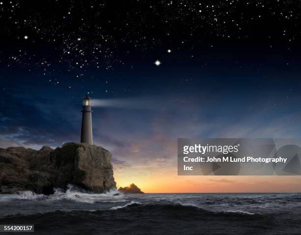 lighthouse beaming over rocky ocean waves under sunrise sky - lighthouse sunset stock pictures, royalty-free photos & images