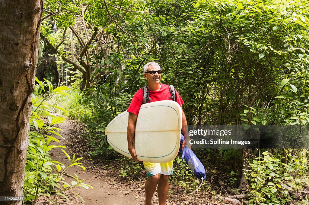 Caucasian man carrying surfboard in jungle