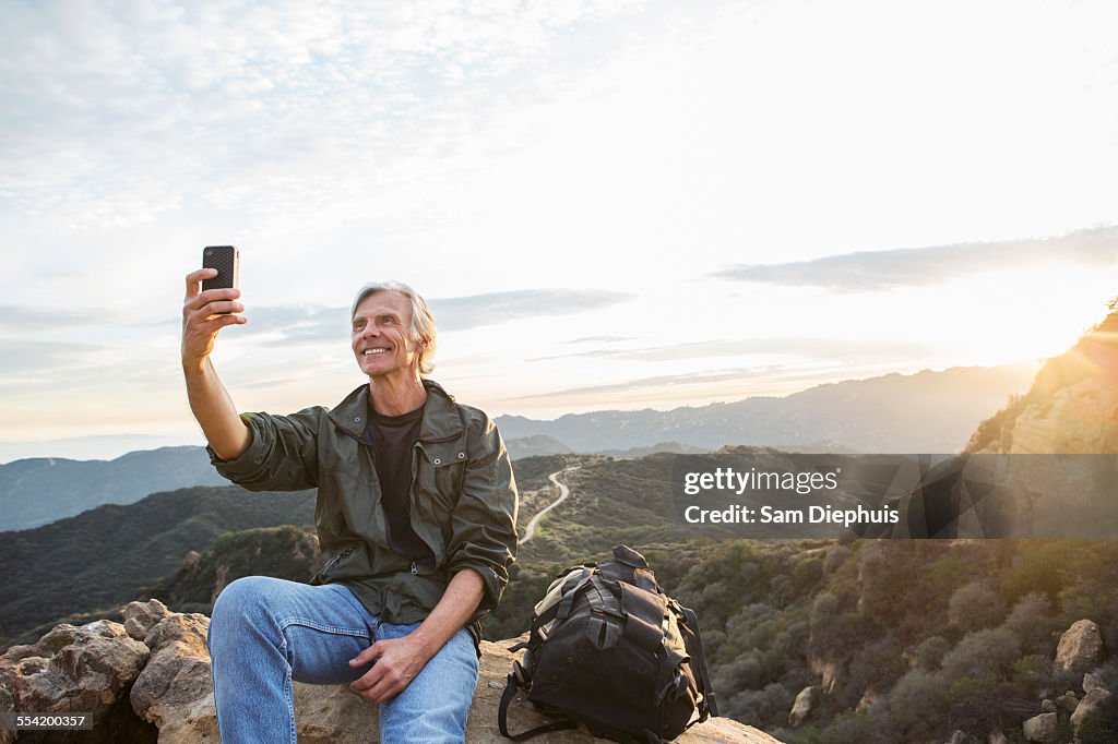 Older Caucasian man taking cell phone photograph on rocky hilltop