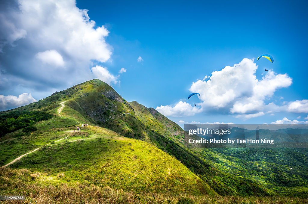 Trail to the hilltop in sunny day with paragliders