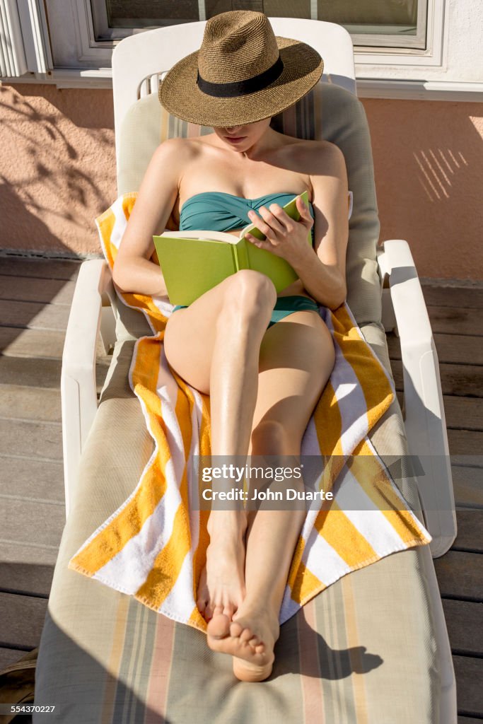 Caucasian woman reading and sunbathing in deck chair