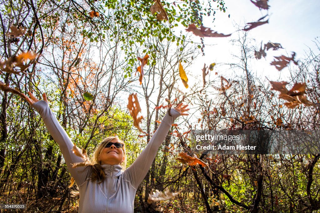 Caucasian woman throwing autumn leaves in forest