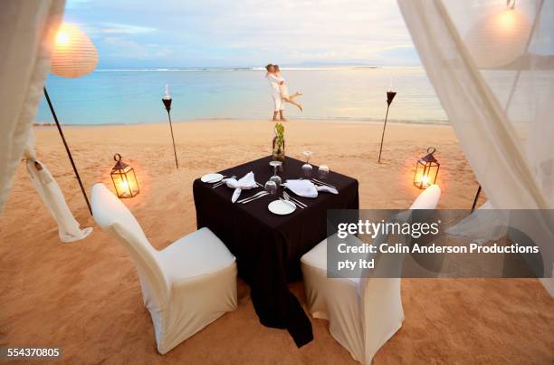 playful couple near table prepared for romantic dinner at beach - candlelight stock pictures, royalty-free photos & images