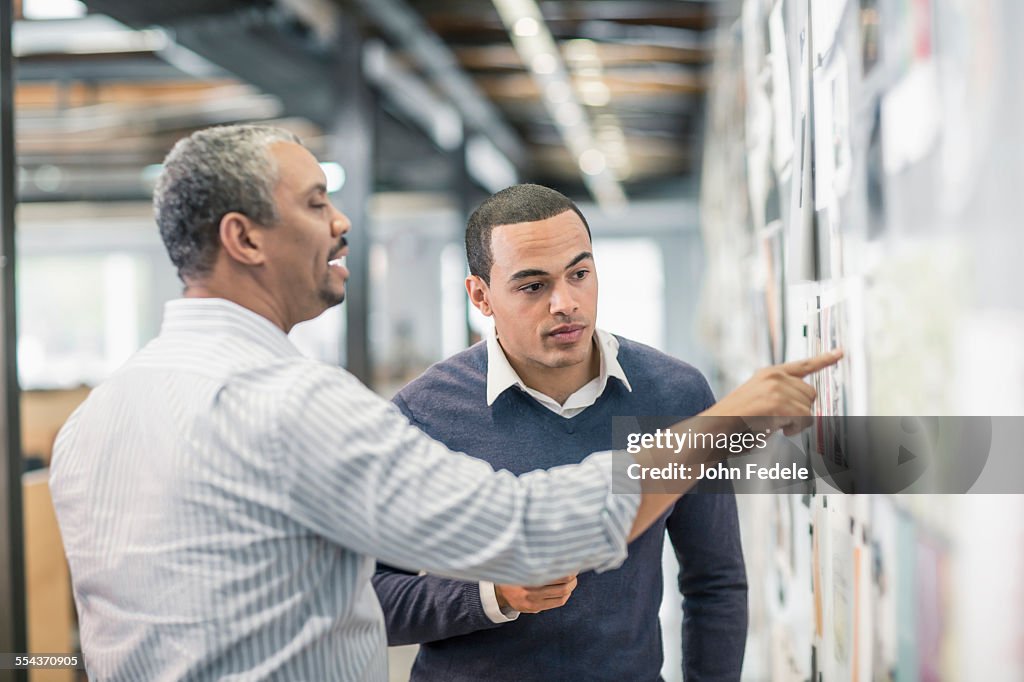 Businessmen examining photographs on wall in office