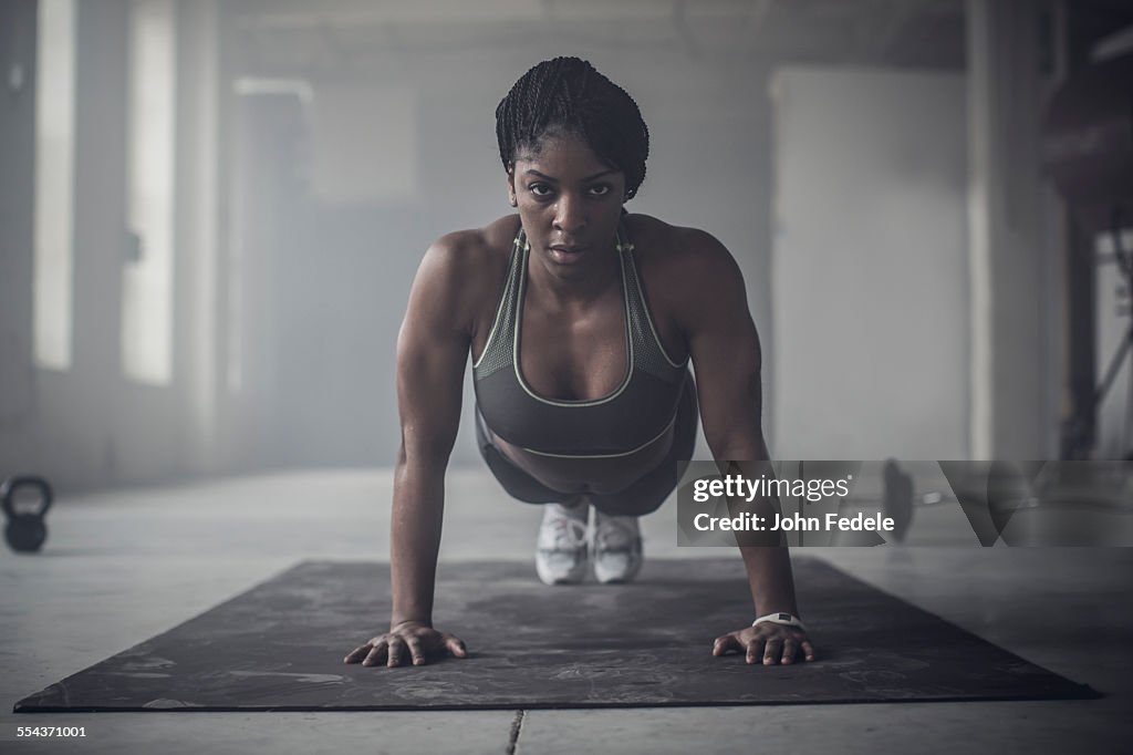 Black woman doing push-ups in dark gym