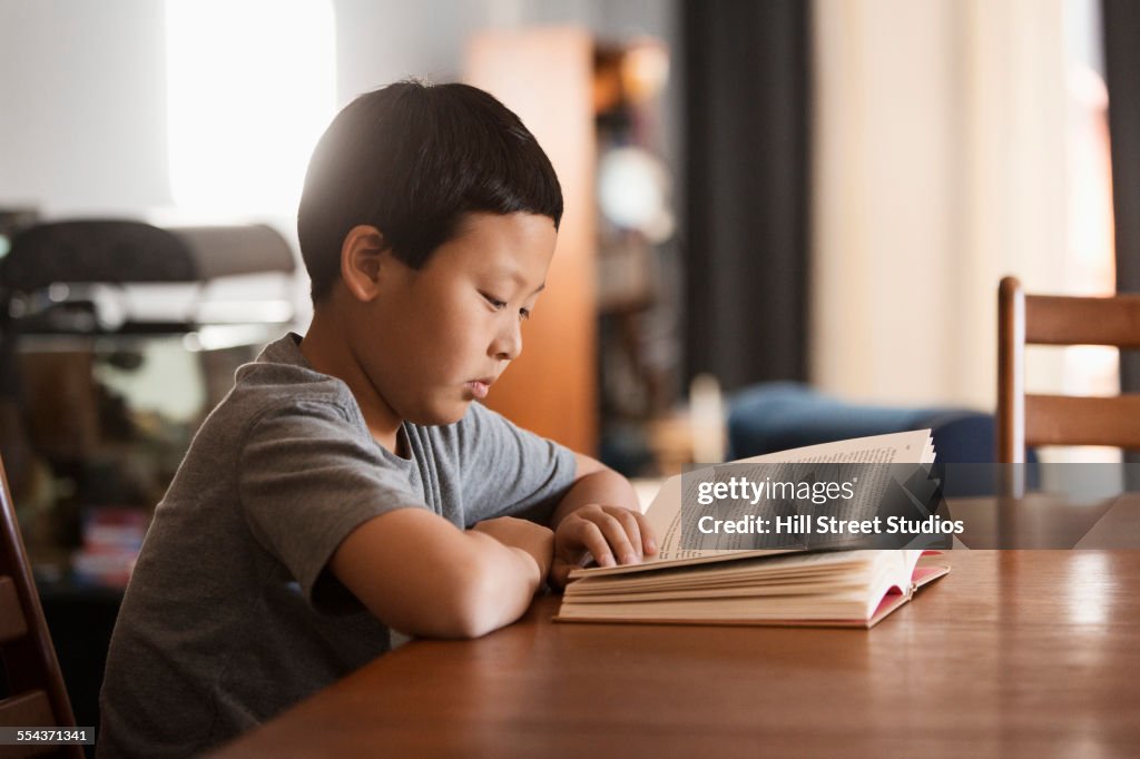 Asian boy reading book at table