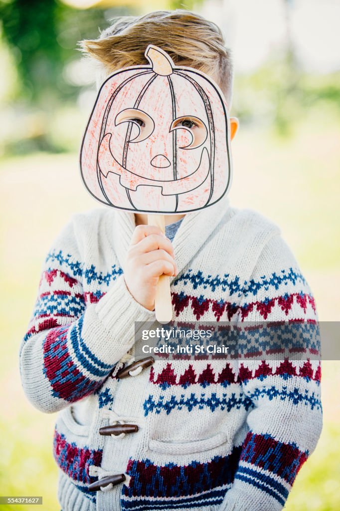 Caucasian boy holding jack-o-lantern mask