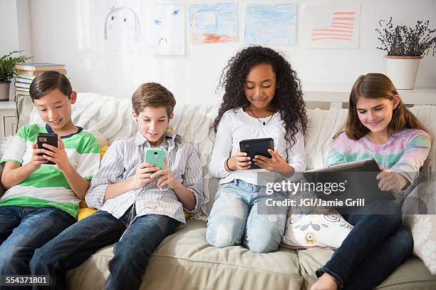 children using cell phones and digital tablets on sofa - children only stock pictures, royalty-free photos & images