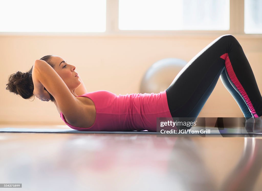 Close up of Hispanic woman doing sit-ups in gym