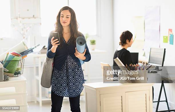 businesswoman carrying yoga mat and cell phone in office - sport office foto e immagini stock