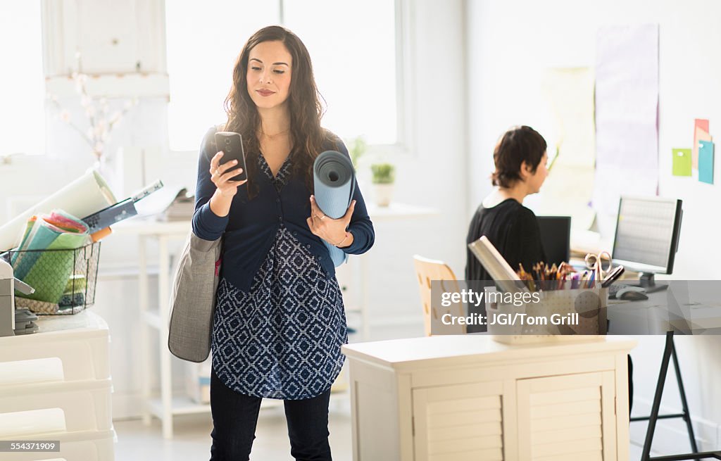 Businesswoman carrying yoga mat and cell phone in office