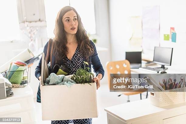 hispanic businesswoman carrying cardboard box in office - downsizing stock-fotos und bilder