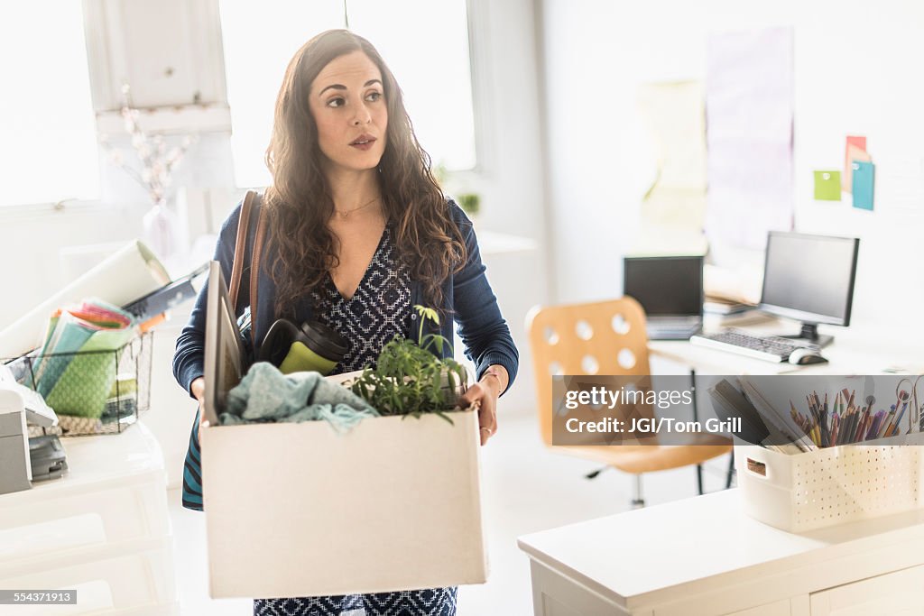 Hispanic businesswoman carrying cardboard box in office