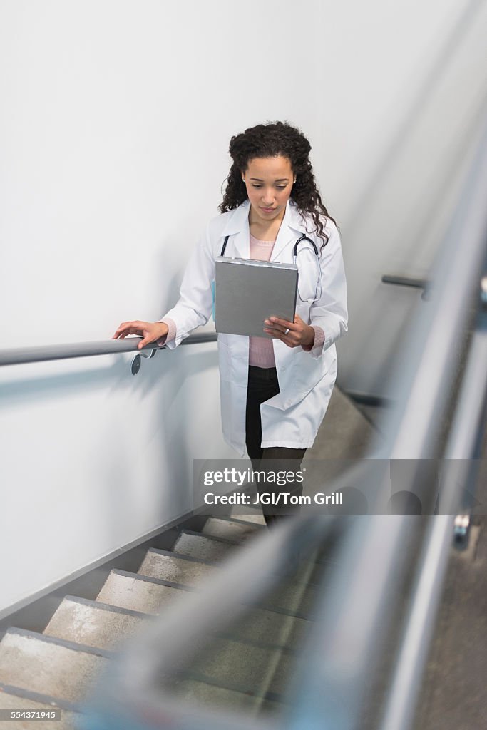 High angle view of mixed race doctor reading medical chart on staircase