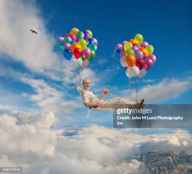 caucasian man on lawn chair floating with balloons in sky - man flying stockfoto's en -beelden