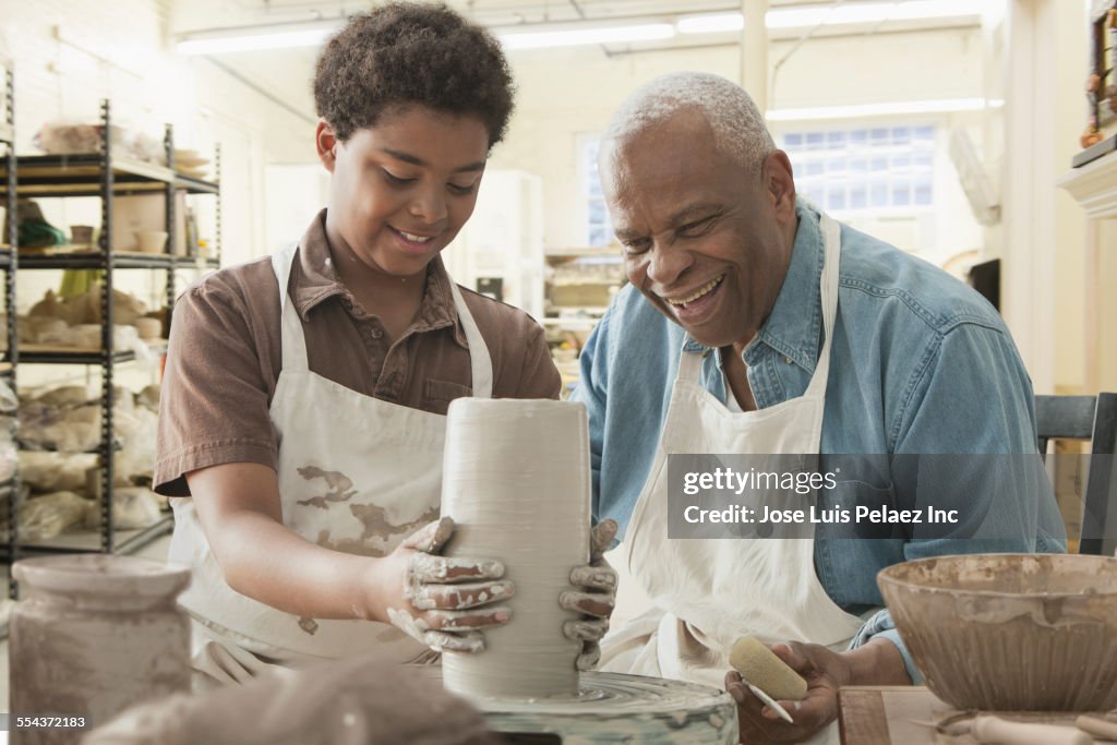 Grandfather and grandson forming pottery on wheel in studio