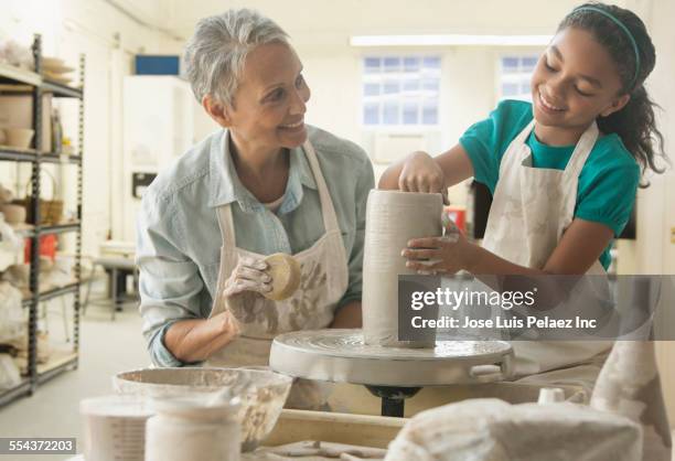 grandmother and granddaughter forming pottery on wheel in studio - african american women wet stock-fotos und bilder