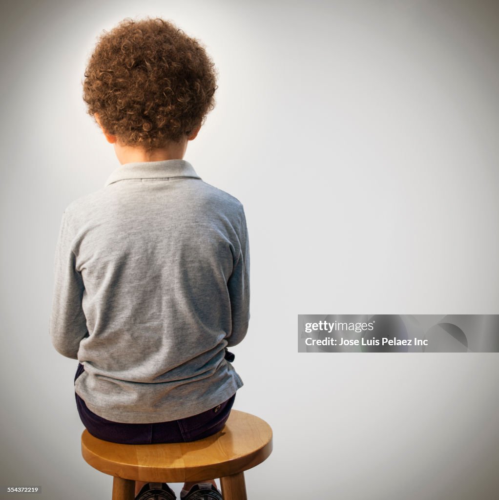 Rear view of mixed race boy sitting on stool