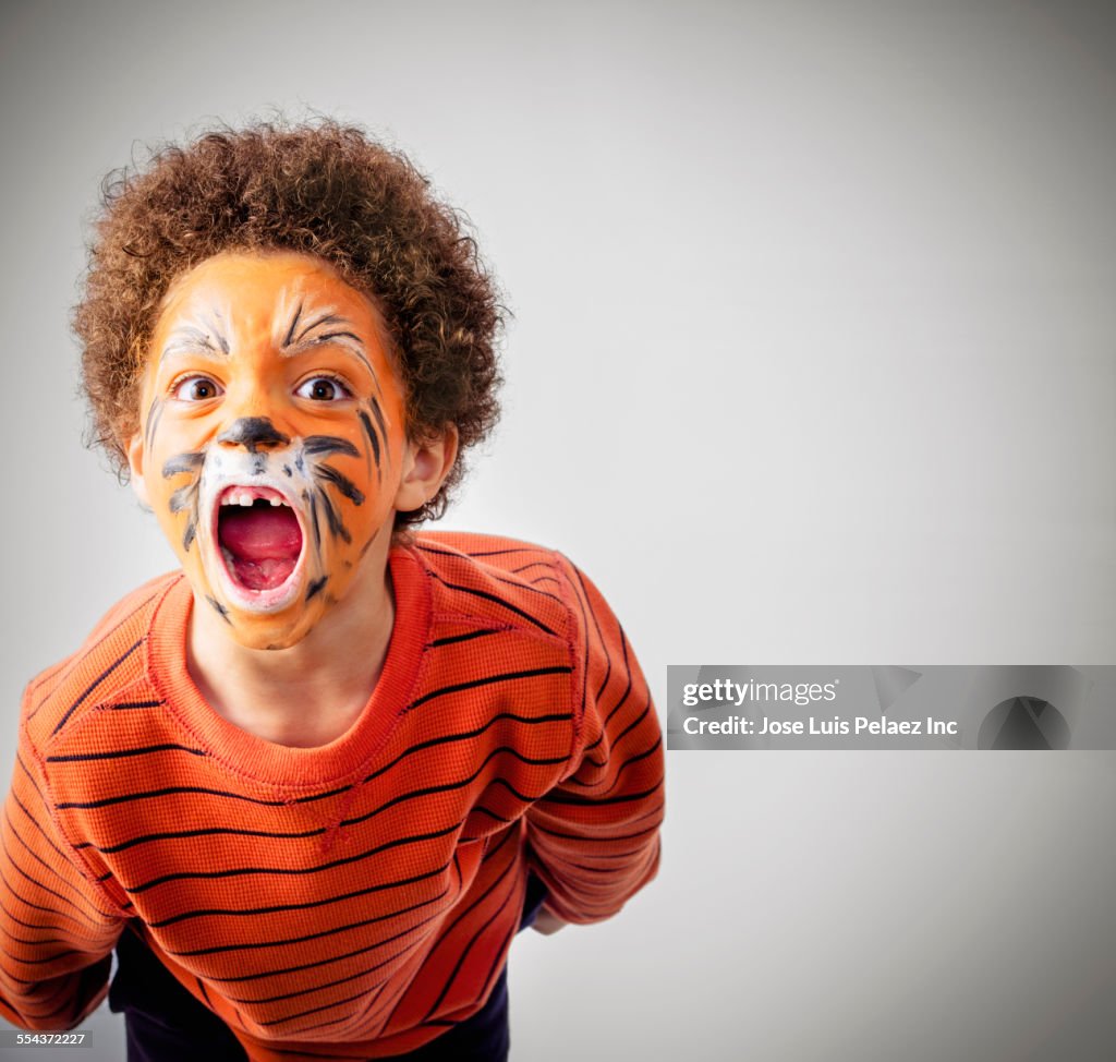 Mixed race boy roaring in tiger face paint