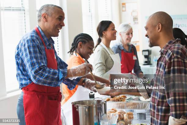 volunteers serving food at community kitchen - soup kitchen stock-fotos und bilder