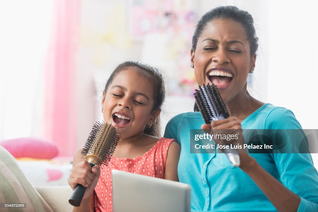 Hispanic mother and daughter singing with hairbrushes and digital tablet