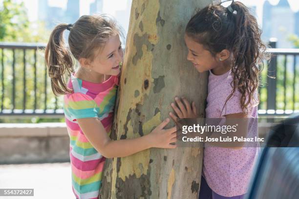 girls peeking around tree in park - children only ponytail stock-fotos und bilder
