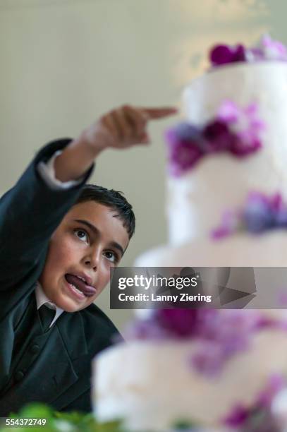 close up of ring bearer sneaking frosting from wedding cake - ring bearer stockfoto's en -beelden