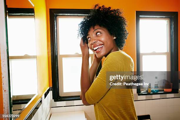 smiling black woman styling hair in bathroom mirror - black woman hair stock pictures, royalty-free photos & images