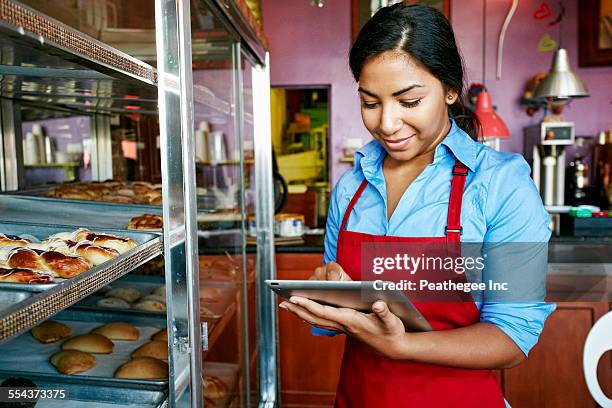 hispanic waitress taking inventory with digital tablet in bakery - america patisserie fotografías e imágenes de stock