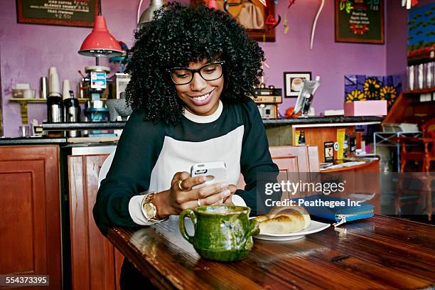 mixed race woman using cell phone in cafe - african american restaurant texting stockfoto's en -beelden