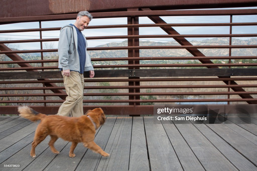 Caucasian man and dog walking on wooden bridge