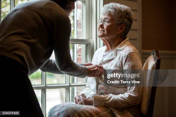 woman buttoning pajamas of mother near window - woman home with sick children stock pictures, royalty-free photos & images