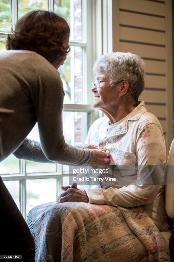 Woman buttoning pajamas of mother near window