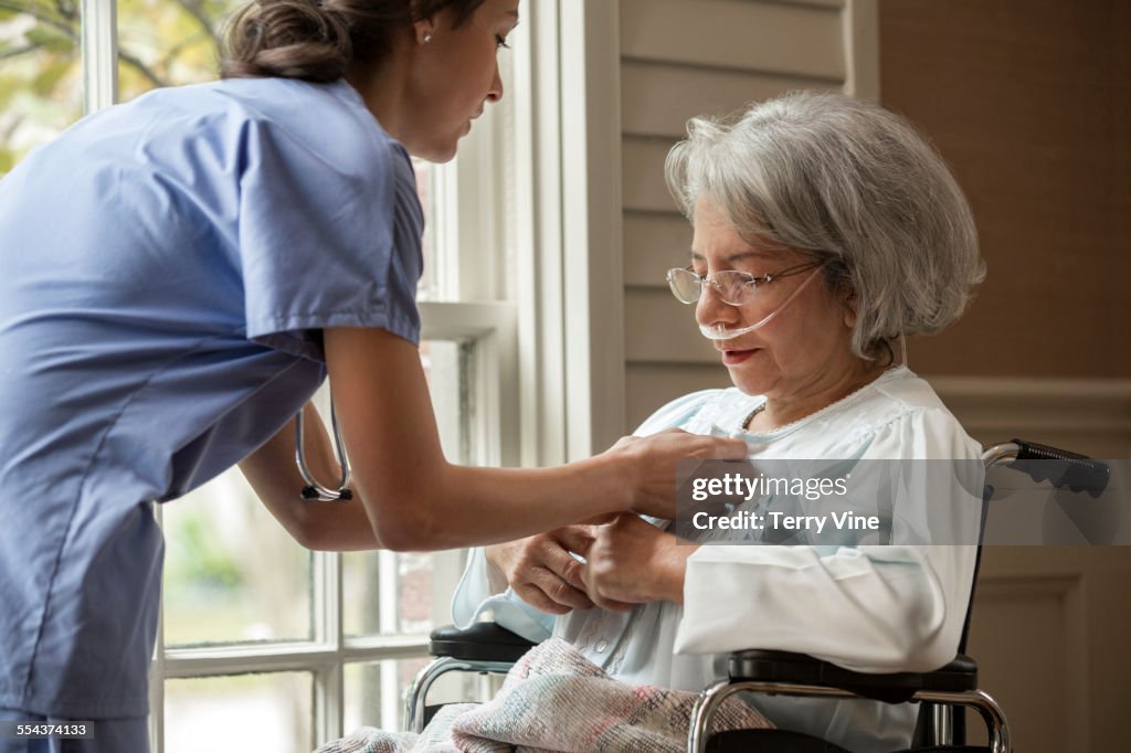 Nurse buttoning shirt of patient in wheelchair near window