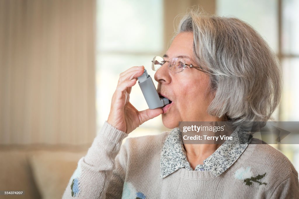 Close up of older Hispanic woman using asthma inhaler