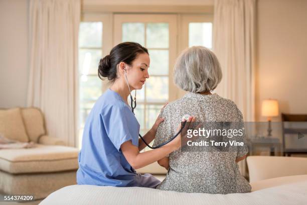nurse listening to chest of patient in home - dr house stock pictures, royalty-free photos & images