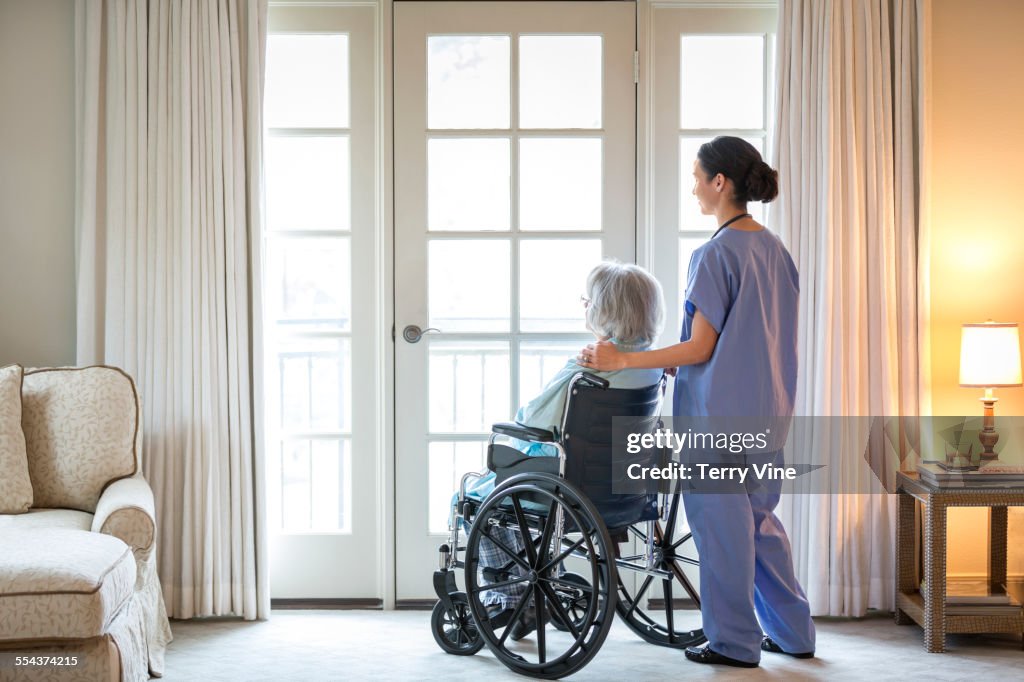 Nurse and older patient in wheelchair standing near window