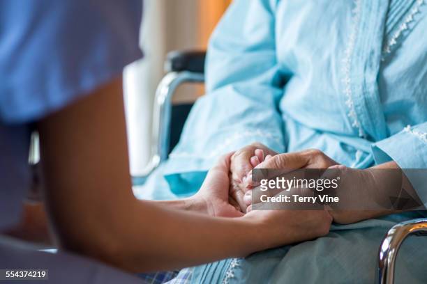 close up of nurse comforting older patient in wheelchair - holding hands close up stock-fotos und bilder