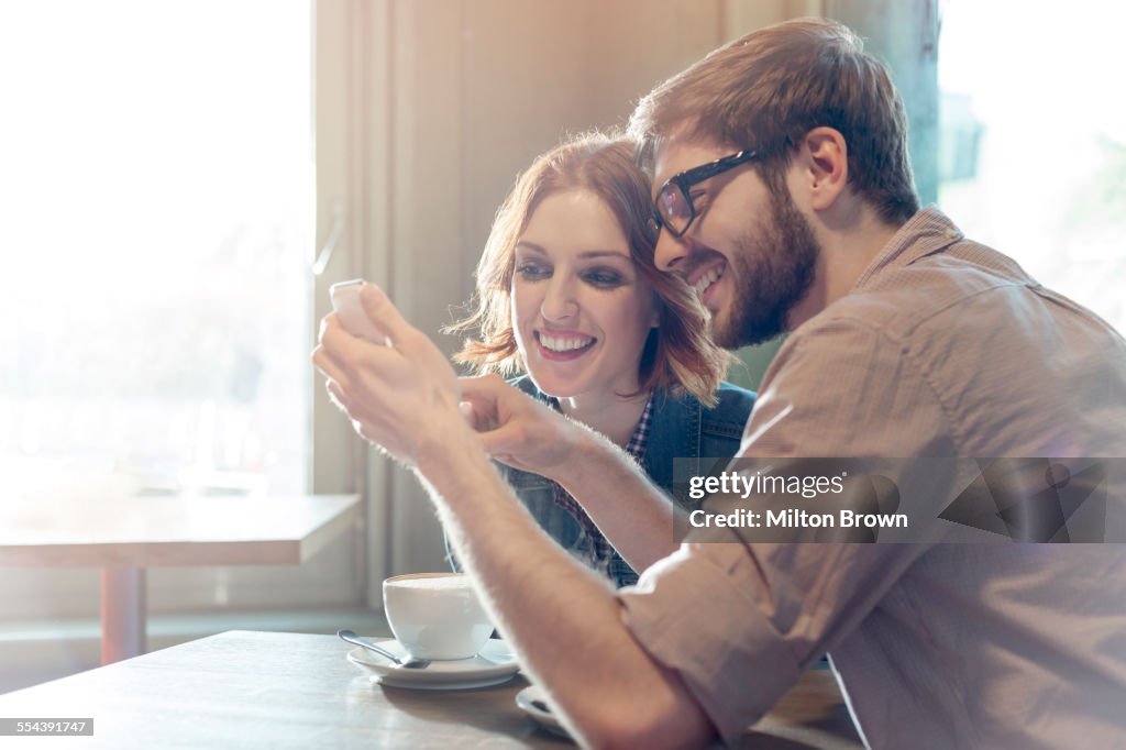 Couple using cell phone in sunny cafe